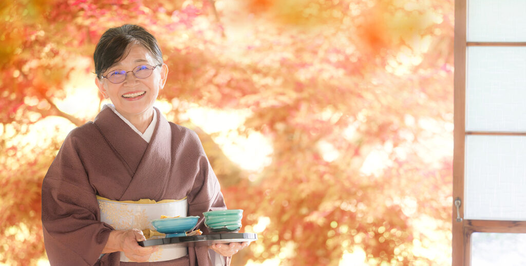 Perfect for autumn travel images. Autumn leaves in the background. Proprietress of long-established ryokan serving food. Looking at the camera. 